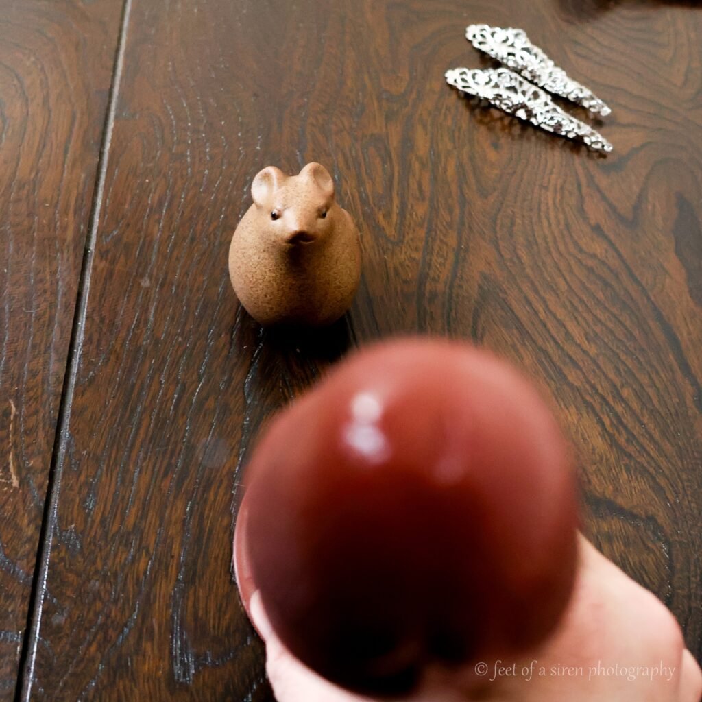 a small dormouse figurine looking towards the viewer, who is holding POV style, a phallic object.