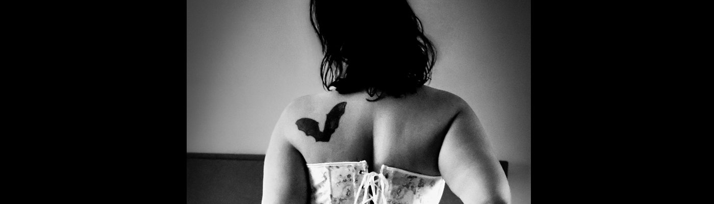 Black and white photograph of a woman in a floral corset facing away from the camera, hair hiding her face.
