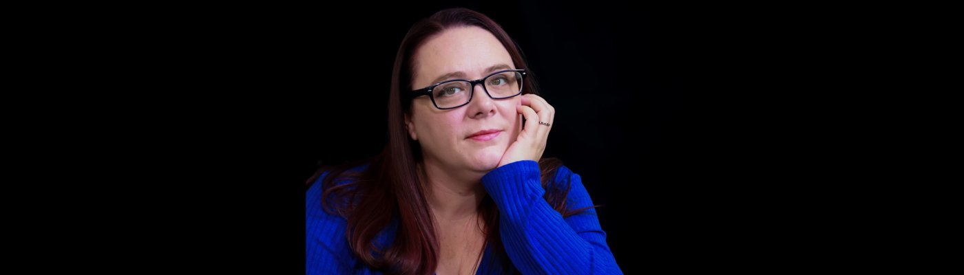 Color photograph portrait of an author wearing a blue dress and glasses. 