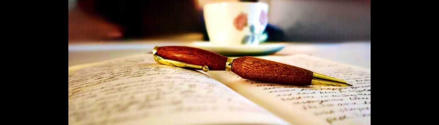 Color photograph of an open journal with a pen across the pages, and a teacup with flowers in the background.