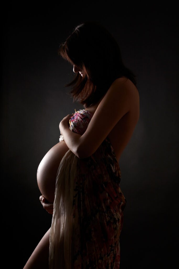 Pregnant person facing to the side, light falling on an exposed belly swollen with childbearing.