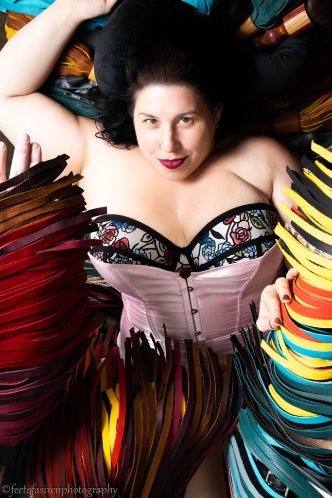 Floggers are a girl's best friend. Woman laying down, surrounded by dozens of flogger falls.